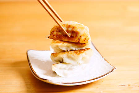 plate of gyoza dumplings with soy sauce and wooden chopstick on wooden table background. Asian food Gyoza or Jiaozi fried dumplings. Selective focus.の写真素材