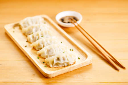 plate of gyoza dumplings with soy sauce and wooden chopstick on wooden table background. Asian food Gyoza or Jiaozi fried dumplings. Selective focus.の写真素材