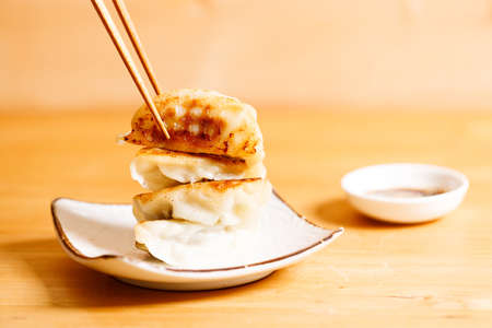 plate of gyoza dumplings with soy sauce and wooden chopstick on wooden table background. Asian food Gyoza or Jiaozi fried dumplings. Selective focus.の写真素材