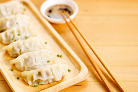 plate of gyoza dumplings with soy sauce and wooden chopstick on wooden table background. Asian food Gyoza or Jiaozi fried dumplings. Selective focus.の写真素材
