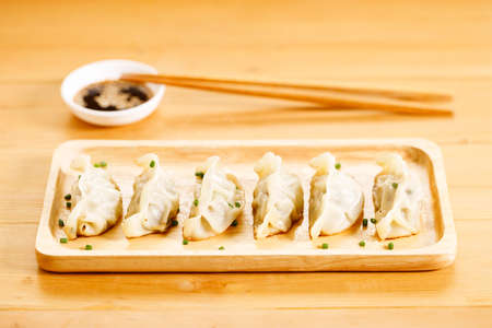 plate of gyoza dumplings with soy sauce and wooden chopstick on wooden table background. Asian food Gyoza or Jiaozi fried dumplings. Selective focus.の写真素材