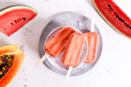 Red watermelon ice cream sticks with sliced fresh watermelon in white bowl with ice on marble table background. Summer food concept.の写真素材