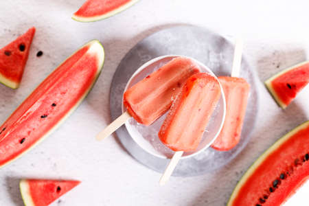 Red watermelon ice cream sticks with sliced fresh watermelon in white bowl with ice on marble table background. Summer food concept.の写真素材