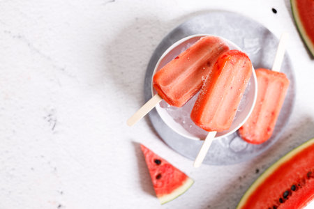 Red watermelon ice cream sticks with sliced fresh watermelon in white bowl with ice on marble table background. Summer food concept.の写真素材