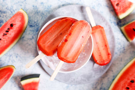 Red watermelon ice cream sticks with sliced fresh watermelon in white bowl with ice on marble table background. Summer food concept.の写真素材