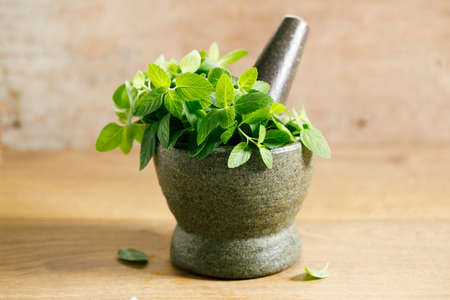 Fresh mint leaves in a stone mortar on wooden table.