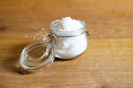 Crystals of sea salt in a glass container laying on a wooden table background. Salted food.の写真素材