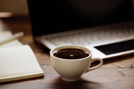 closeup a cup of coffee with laptop background on wooden desk. Home office concept.の写真素材