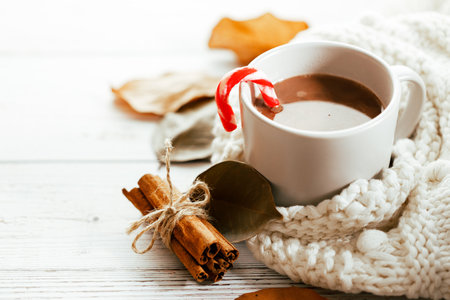 Cup of hot chocolate with candy cane on wooden table with white scarf. Closeup.の写真素材
