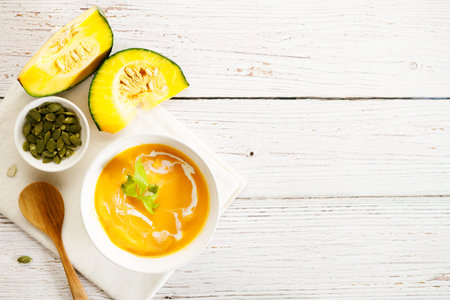 Pumpkin soup with pumpkin seeds and cream. Pumpkin soup in a white bowl on wooden table background with copy space.の写真素材