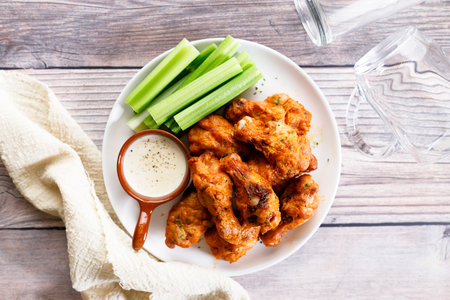 Grilled spicy chicken wings with dipping sauce and celery on a white plate on wooden table background.の写真素材