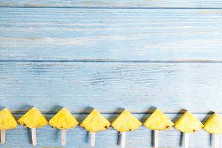Pineapple sticks, sliced juicy pineapples with wooden sticks, on blue wooden background in tropical concept.の写真素材