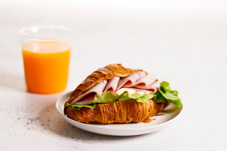 Fresh baked croissant sandwich with ham, cheese and lettuce on white plate. Healthy breakfast.の写真素材