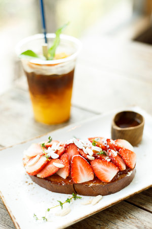 Strawberry toast with toasted bread, sliced fresh strawberries and honey on white plate on wooden table.の写真素材