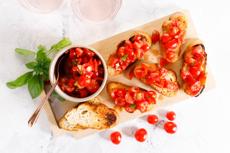 Delicious savory Italian tomato bruschetta slices on white wooden board. Tomato bruschetta with chopped tomatoes, garlic and herbs on toasted bread.の写真素材