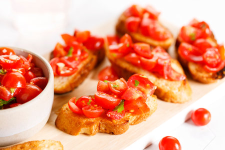 Delicious savory Italian tomato bruschetta slices on white wooden board. Tomato bruschetta with chopped tomatoes, garlic and herbs on toasted bread.の写真素材