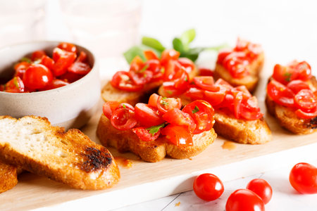 Delicious savory Italian tomato bruschetta slices on white wooden board. Tomato bruschetta with chopped tomatoes, garlic and herbs on toasted bread.の写真素材