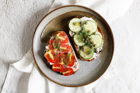 Toasted sliced breads with cream cheese topped with fresh cucumber and cherry tomato. Healthy fresh vegetable toast for breakfast.の写真素材