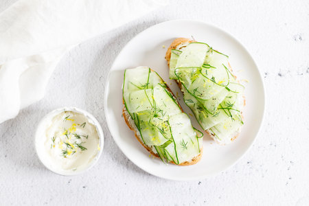 Sliced cucumber sandwiches with soft cheese and topped with chopped dill and lemon zest. Vegetarian breakfast dish. Closeup.の写真素材