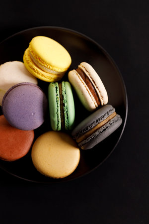 Colorful macaron cookies on black color plate. Sweet French macarons in different colors. Closeup.の写真素材