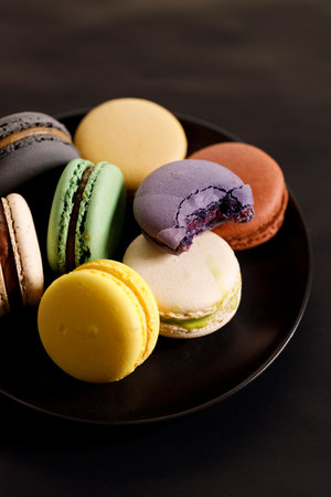 Colorful macaron cookies on black color plate. Sweet French macarons in different colors. Closeup.の写真素材