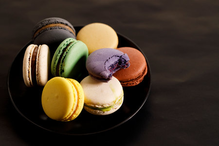 Colorful macaron cookies on black color plate. Sweet French macarons in different colors. Closeup.の写真素材