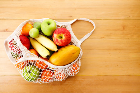 Fresh fruits in reusable grocery net bag on wooden table. Apple, banana, papaya, orange and lime in eco cotton bag. Zero waste, plastic-free and sustainable lifestyle.の写真素材