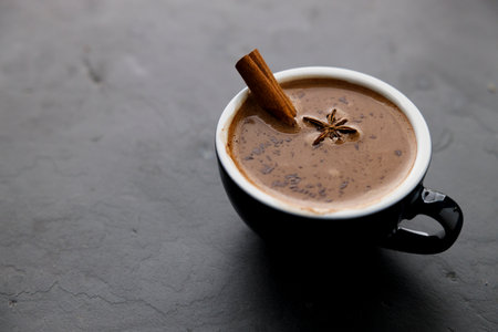 Spicy hot chocolate with cinnamon in ceramic blue cup on dark stone background.の写真素材