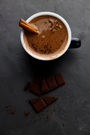 Spicy hot chocolate with cinnamon in ceramic blue cup on dark stone background.の写真素材
