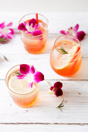 Summer cocktail in glasses with sliced lemon and pink orchid flower on wooden table background. Concept of fresh summer drinks.の写真素材