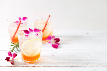 Summer cocktail in glasses with sliced lemon and pink orchid flower on wooden table background. Concept of fresh summer drinks.の写真素材