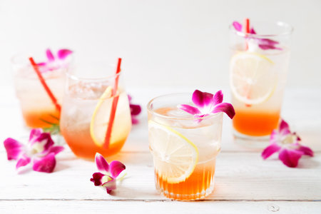Summer cocktail in glasses with sliced lemon and pink orchid flower on wooden table background. Concept of fresh summer drinks.の写真素材