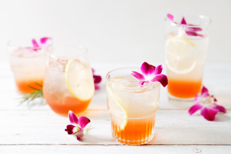 Summer cocktail in glasses with sliced lemon and pink orchid flower on wooden table background. Concept of fresh summer drinks.の写真素材
