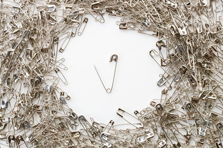 Silver safety pins with big and small size scattered on white background.