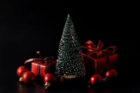 Miniature snowy Christmas tree with red present boxes decorated in bow on black background. Christmas and New year concept.の写真素材