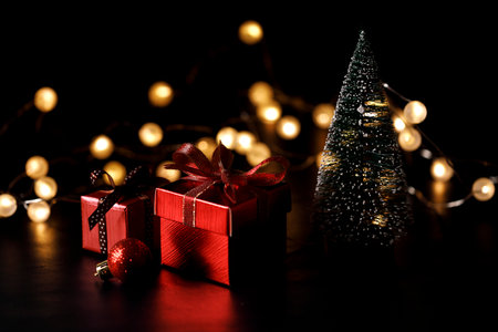 Miniature snowy Christmas tree with red present boxes decorated in bow on black background. Christmas and New year concept.の写真素材
