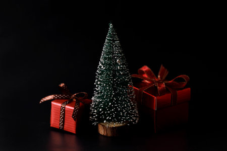 Miniature snowy Christmas tree with red present boxes decorated in bow on black background. Christmas and New year concept.の写真素材