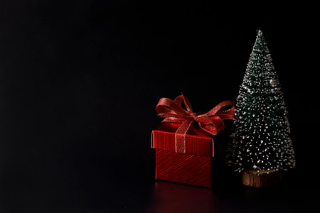 Miniature snowy Christmas tree with red present box decorated in bow on black background. Christmas and New year concept.の写真素材