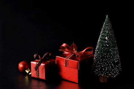 Miniature snowy Christmas tree with red present boxes decorated in bow on black background. Christmas and New year concept.の写真素材