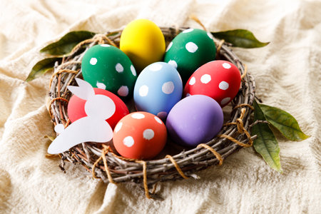 Easter eggs painted in white dot pattern in small wooden nest on white wooden table. Colorful Easter decoration.の写真素材