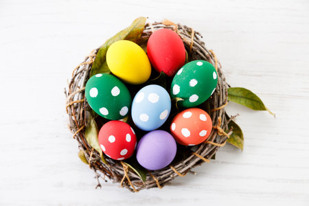 Easter eggs painted in white dot pattern in small wooden nest on white wooden table. Colorful Easter decoration.の写真素材