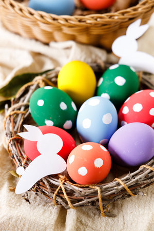 Easter eggs painted in white dot pattern in small wooden nest on white wooden table. Colorful Easter decoration.の写真素材