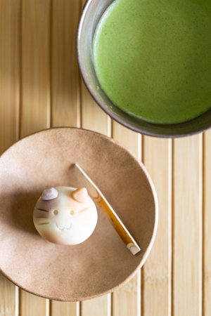 Fresh matcha drink in traditional ceramic bowl with traditional Japanese confection in shape of cat on wooden table background. Green tea drink in contemporary concept.の写真素材