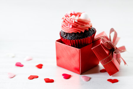 Chocolate cupcake with pink color buttercream in red present box on white wooden background. Sweet and love concept. Happy Valentines day concept.の写真素材