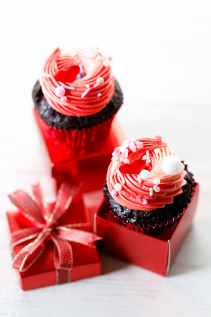Chocolate cupcakes with pink color buttercream in red present box on white wooden background. Sweet and love concept. Happy Valentines day concept.の写真素材