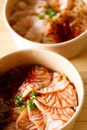 Closeup of Japanese rice bowl with seared sliced salmon in paper container on wooden table.の写真素材