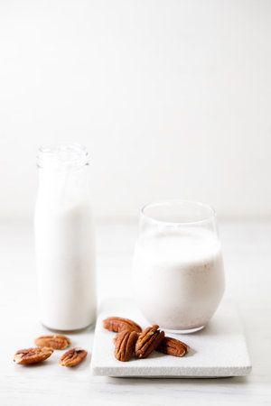 Pecan milk in a glass with raw pecan nuts on wooden table. Homemade dairy-free milk.