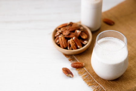 Pecan milk in a glass with raw pecan nuts on wooden table. Homemade dairy-free milk.