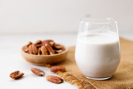 Pecan milk in a glass with raw pecan nuts on wooden table. Homemade dairy-free milk.の写真素材