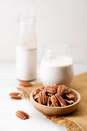 Pecan milk in a glass with raw pecan nuts on wooden table. Homemade dairy-free milk.の写真素材